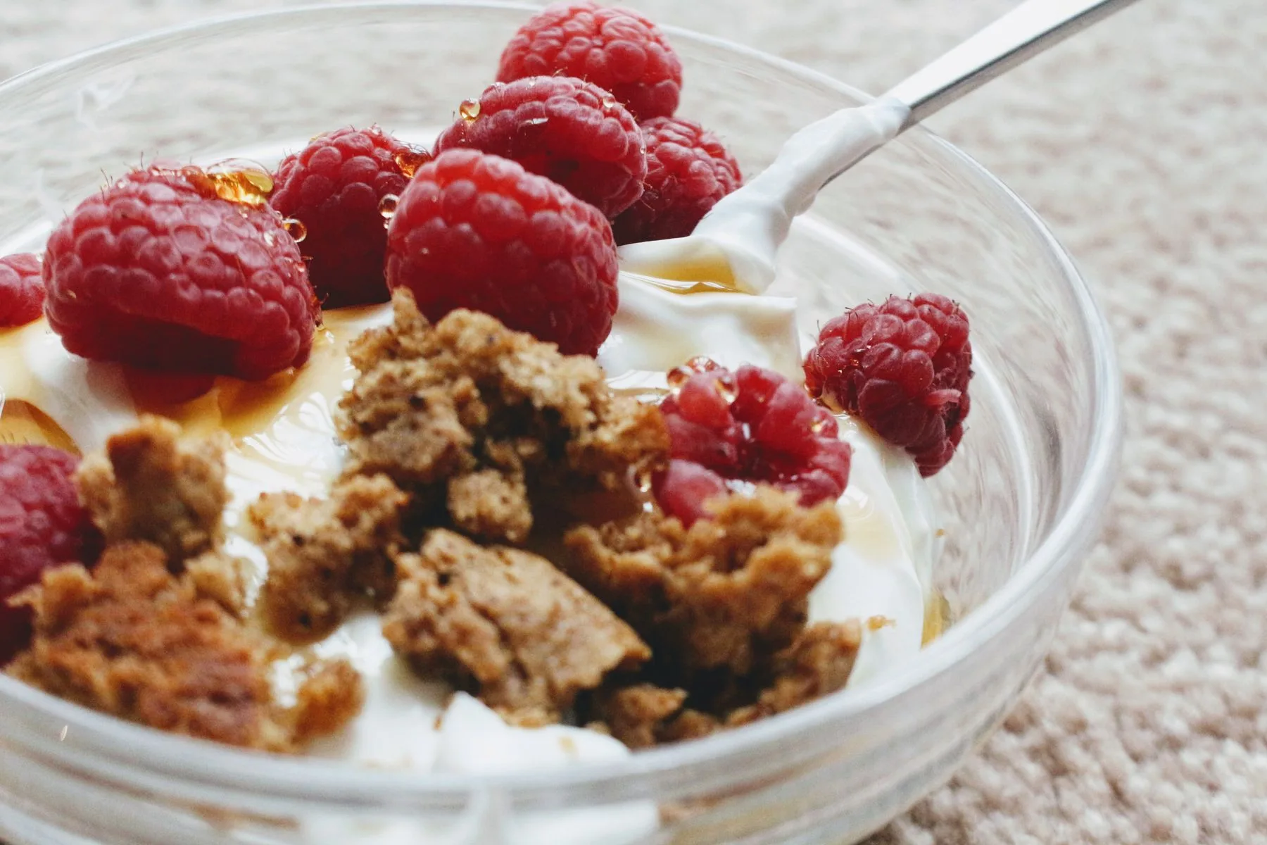 Tykk naturell yoghurt med bringebær og sprø topping i en glasskål